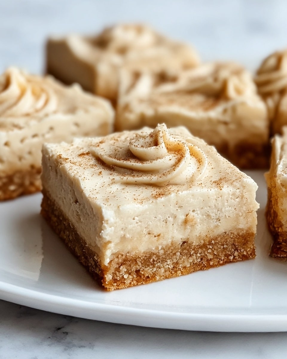 A close-up of a square dessert bar on a white plate, showing two distinct layers: the bottom layer is a crunchy, grainy, golden-brown crust, while the top layer is a thick, creamy, light beige filling with a rough texture, decorated with soft swirls and light brown sprinkles on top. The dessert bar is cut into neat squares, and the white plate contrasts with the textured layers, all placed on a white marbled surface. photo taken with an iphone --ar 4:5 --v 7
