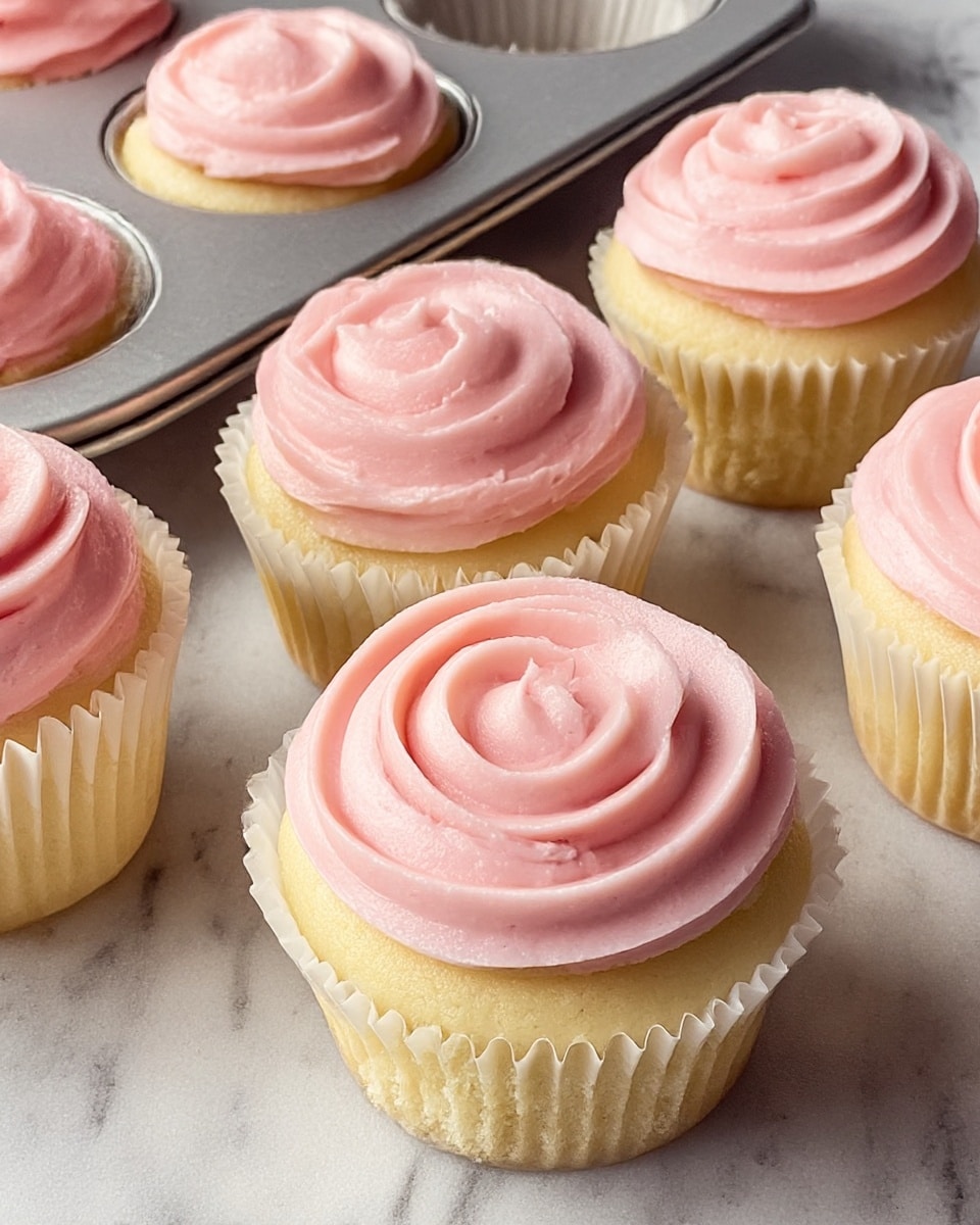 The image shows six vanilla cupcakes with a soft yellow base, each wrapped in white paper liners, topped with a thick swirl of smooth light pink frosting. The frosting has a creamy, slightly glossy texture, and each swirl sits gently on top of the cupcake, covering almost all the surface of the cake but not overflowing. The cupcakes are placed on a white marbled textured surface, and a metal cupcake tray is partially visible with some cupcakes still inside. The overall look is fresh and inviting, highlighting the softness of the cake and the delicate pink color of the frosting. photo taken with an iphone --ar 4:5 --v 7