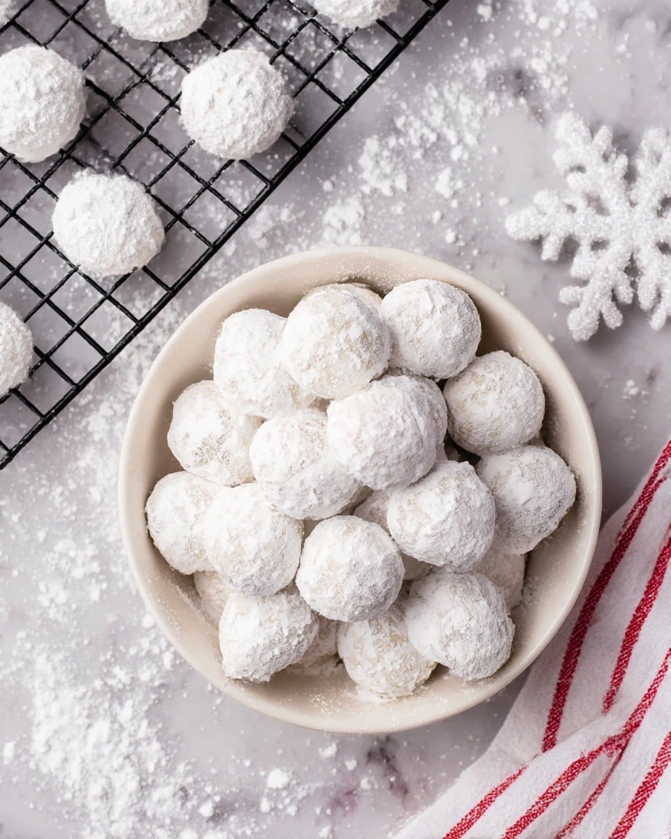 A bowl full of round snowball cookies covered in white powdered sugar sits in the center, with about two layers of cookies piled in the off-white bowl. To the top left, a black cooling rack holds more cookies spaced out, all coated in powdered sugar. The surface underneath is a white marbled texture with powdered sugar scattered across it. To the right of the bowl, a white snowflake-shaped decoration is lightly dusted with powdered sugar. A white cloth with red stripes is partially visible in the bottom right corner. photo taken with an iphone --ar 4:5 --v 7