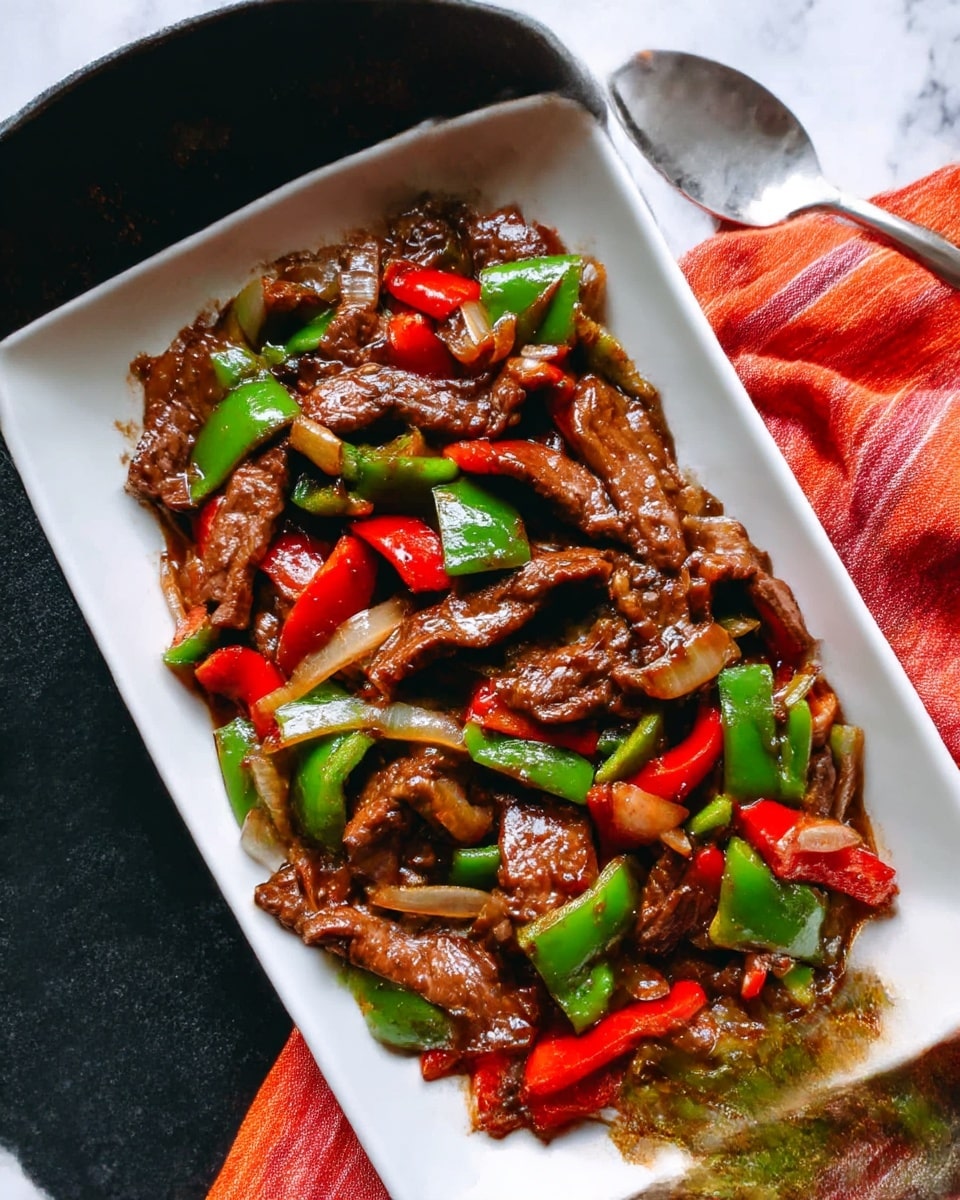 The image shows a white rectangular plate filled with a stir-fry dish made of glistening brown beef slices, chunky green bell pepper pieces, bright red bell pepper pieces, and translucent cooked onion slices, all mixed together in a glossy sauce. The beef slices are layered unevenly on top, while the colorful vegetables are spread throughout, creating a vibrant mix of reds, greens, and browns. Resting on the left side of the plate are a pair of brown chopsticks with lighter tips, and on the right side, a silver spoon is partially visible. The plate is placed on a black surface covered with a white marbled texture and next to a striped orange and red cloth. Photo taken with an iphone --ar 4:5 --v 7