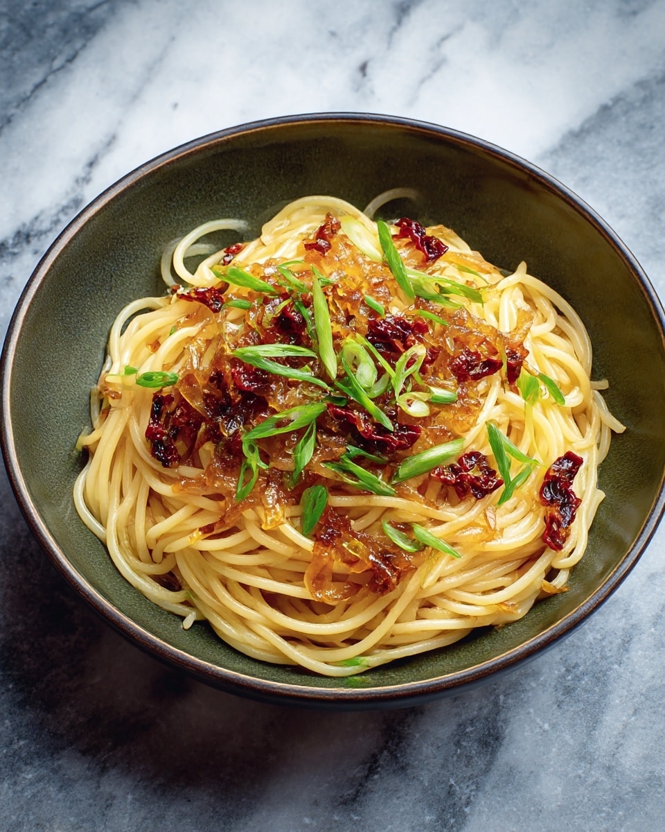 A bowl with a dark olive green inside holds a pile of light yellow spaghetti noodles as the base layer, topped with a glossy, golden-brown layer of caramelized onions. Scattered throughout are small pieces of dark red sun-dried tomatoes, adding color and texture contrast. Bright green slices of fresh scallions are sprinkled evenly on top for a fresh touch. The bowl is set on a white marbled surface. photo taken with an iphone --ar 4:5 --v 7