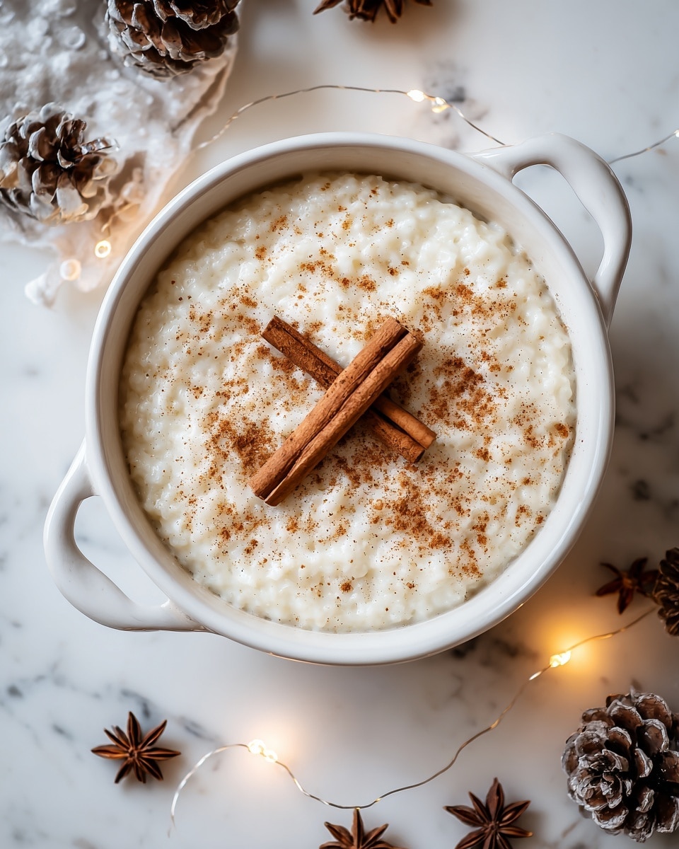 A creamy white rice pudding with a thick, slightly grainy texture fills a round white bowl with handles on both sides. The surface of the pudding is sprinkled evenly with a light brown cinnamon powder, and two whole cinnamon sticks lie crossed in the center. The bowl sits on a white marbled surface, surrounded by small fairy lights and natural elements like pine cones and star anise, adding a warm, cozy touch. Photo taken with an iphone --ar 4:5 --v 7