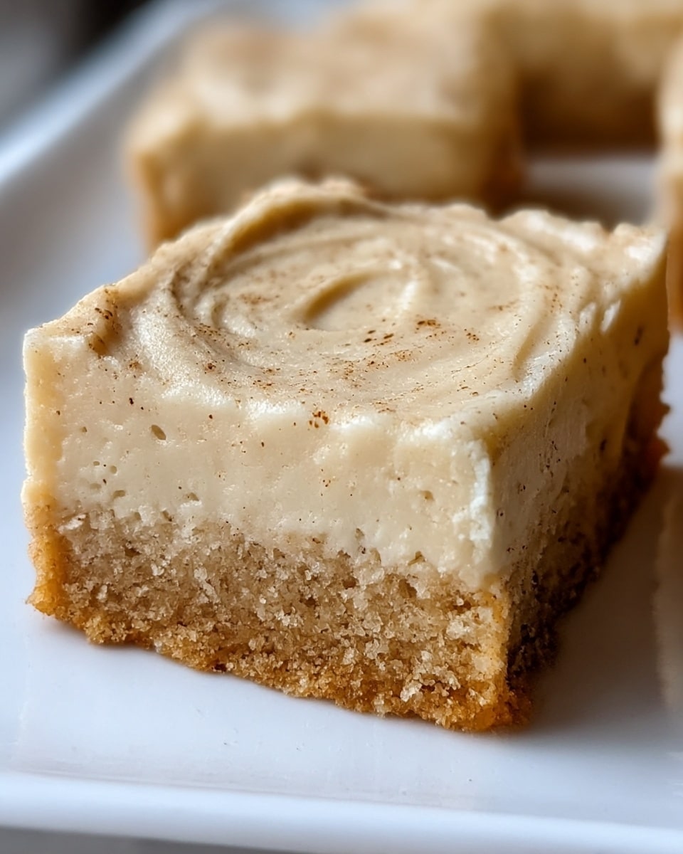 The image shows a close-up of a square dessert bar with two distinct layers placed on a white plate. The bottom layer is a thick, crumbly crust of golden brown color with a grainy texture. Above it, the top layer is thicker, creamy, and light beige, with a smooth but slightly grainy surface that has some swirls and small darker specks sprinkled across it. The dessert edges are slightly rough and the top surface has a soft, almost frosting-like appearance. Photo taken with an iphone --ar 4:5 --v 7
