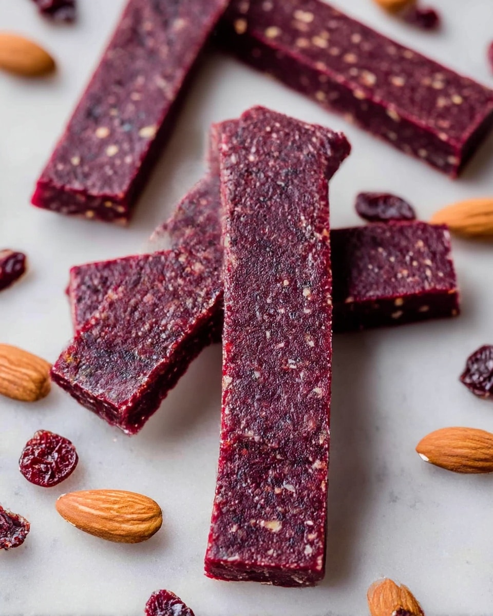 The image shows several rectangular berry and nut snack bars arranged on a white marbled surface. The bars are thick with a dense, dark purplish-red color, and visible small bits of nuts and dried fruit are embedded throughout each bar, giving them a slightly textured look. They are neatly cut with clean edges, lying flat with some almonds and dried cranberries scattered around them, adding natural contrasting colors of light brown and deep red. The overall presentation is simple and rustic, highlighting the natural ingredients in the bars. Photo taken with an iphone --ar 4:5 --v 7
