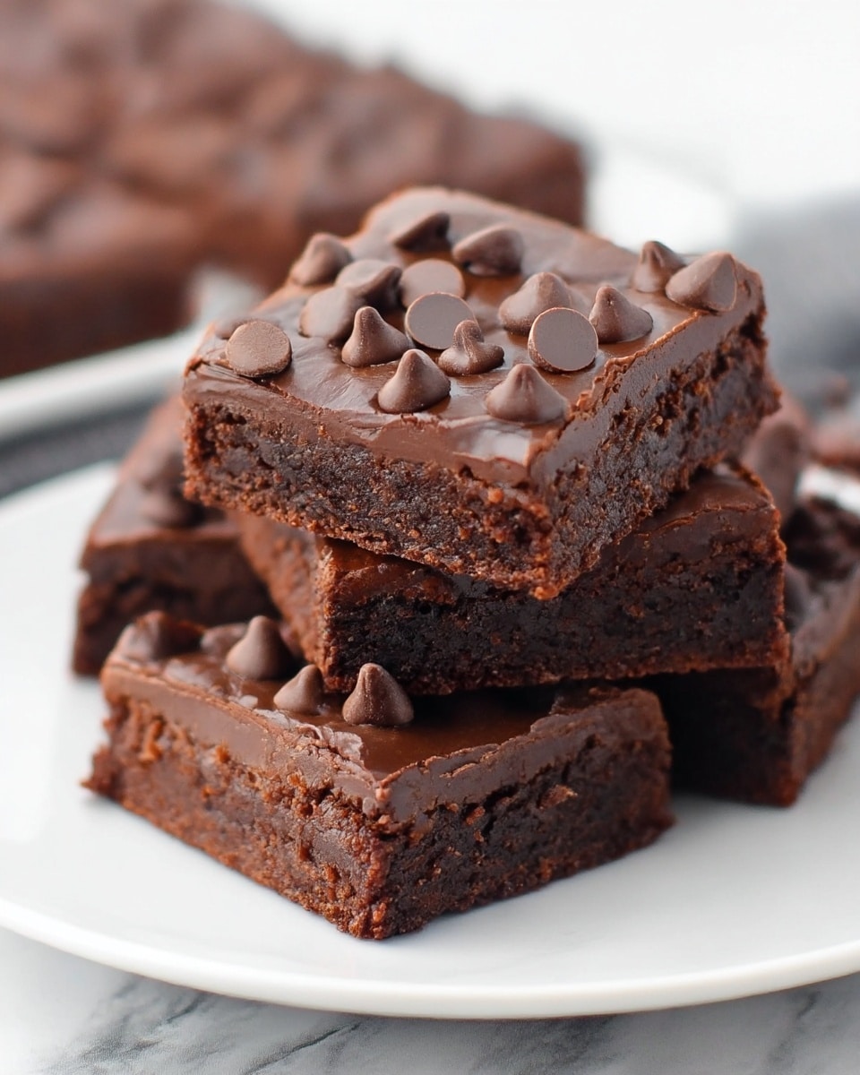 A stack of chocolate brownies sits on a white plate placed on a white marbled surface. Each brownie is square-shaped with two visible layers: a dense, dark brown base and a glossy, thick chocolate topping covered with lighter milk chocolate chips scattered unevenly on top. The brownies have a slightly crumbly texture at the edges but look moist in the middle, and the chips add a rough, uneven texture to the smooth top layer. Photo taken with an iphone --ar 4:5 --v 7