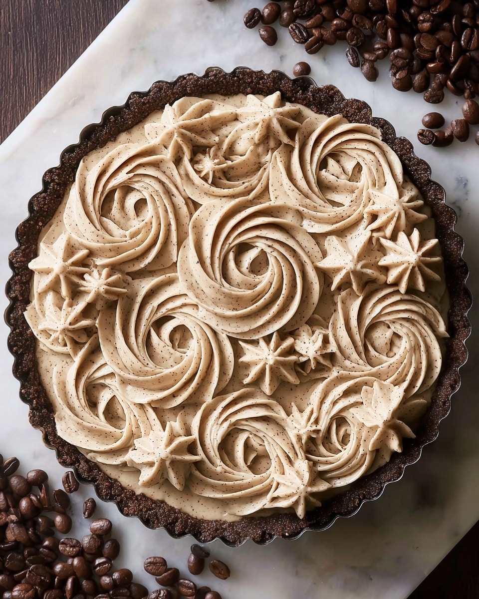 A tart with a dark brown crumbly crust forms the base, pressed into a scalloped white tart pan. On top, a creamy light brown layer is decorated with large swirls and smaller star-shaped dollops of frosting, all textured with subtle specks that hint at spices. The swirls fill most of the surface in a circular pattern, with the stars filling the spaces between. The tart sits on a white marbled surface scattered with shiny, dark brown coffee beans around the edges. photo taken with an iphone --ar 4:5 --v 7