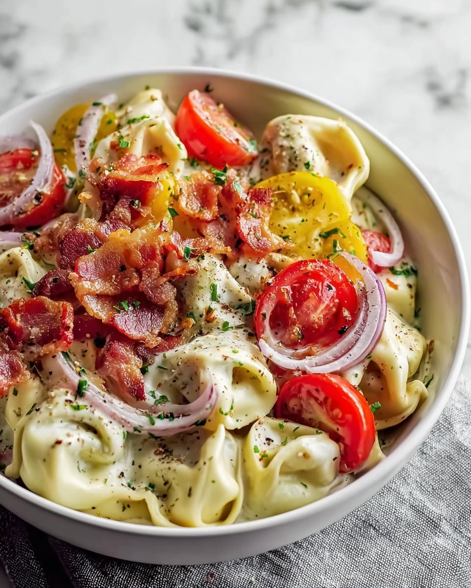 A white bowl filled with three layers of food: the base layer is creamy white tortellini pasta with smooth, folded texture, the middle layer has red cherry tomato halves and thin, curved slices of light purple onions, and the top layer is scattered with crispy, reddish-brown bacon pieces along with thin yellow pepper strips, all sprinkled with green herbs and black pepper. The bowl sits on a light gray cloth on a white marbled surface photo taken with an iphone --ar 4:5 --v 7