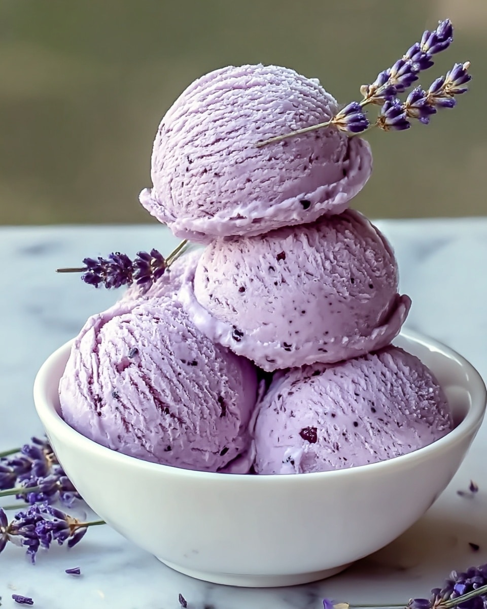 A white bowl holds four scoops of light purple ice cream with small dark specks spread evenly throughout, stacked in a pyramid shape. On top, there are several sprigs of dried lavender flowers, adding a touch of purple and brown contrast. The bowl rests on a white plate with a few lavender flowers scattered around its base. The background is soft green and blurred, while the bowl and plate sit on a white marbled surface. photo taken with an iphone --ar 4:5 --v 7