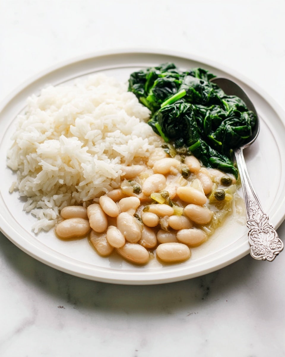 A white plate holds a serving of three food layers arranged side by side: on the left is a mound of soft white rice with fluffy texture, in the middle there is a creamy bean stew made of light beige beans coated in a glossy sauce with small bits of celery and capers, and on the right are dark green cooked spinach leaves that look slightly glossy and tender. A silver spoon with floral engraving rests on the edge of the plate, touching the spinach. The plate sits on a white marbled surface. photo taken with an iphone --ar 4:5 --v 7