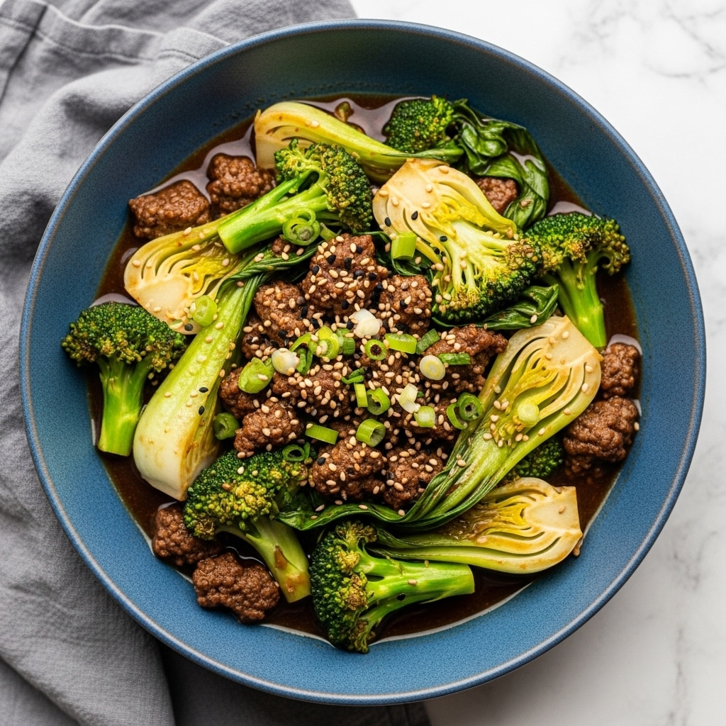 A blue bowl with a slightly rough edge holds a stir-fry made of several layers: the bottom layer is a dark, glossy sauce, topped with pieces of cooked ground beef that are brown and textured. Mixed among the beef are bright green broccoli florets and light yellow slices of bok choy, both appearing tender and slightly shiny from the sauce. Small, pale sesame seeds and chopped green onions are sprinkled across the top, adding texture and color contrast. The bowl sits on a gray cloth on a white marbled surface. Photo taken with an iphone --ar 4:5 --v 7