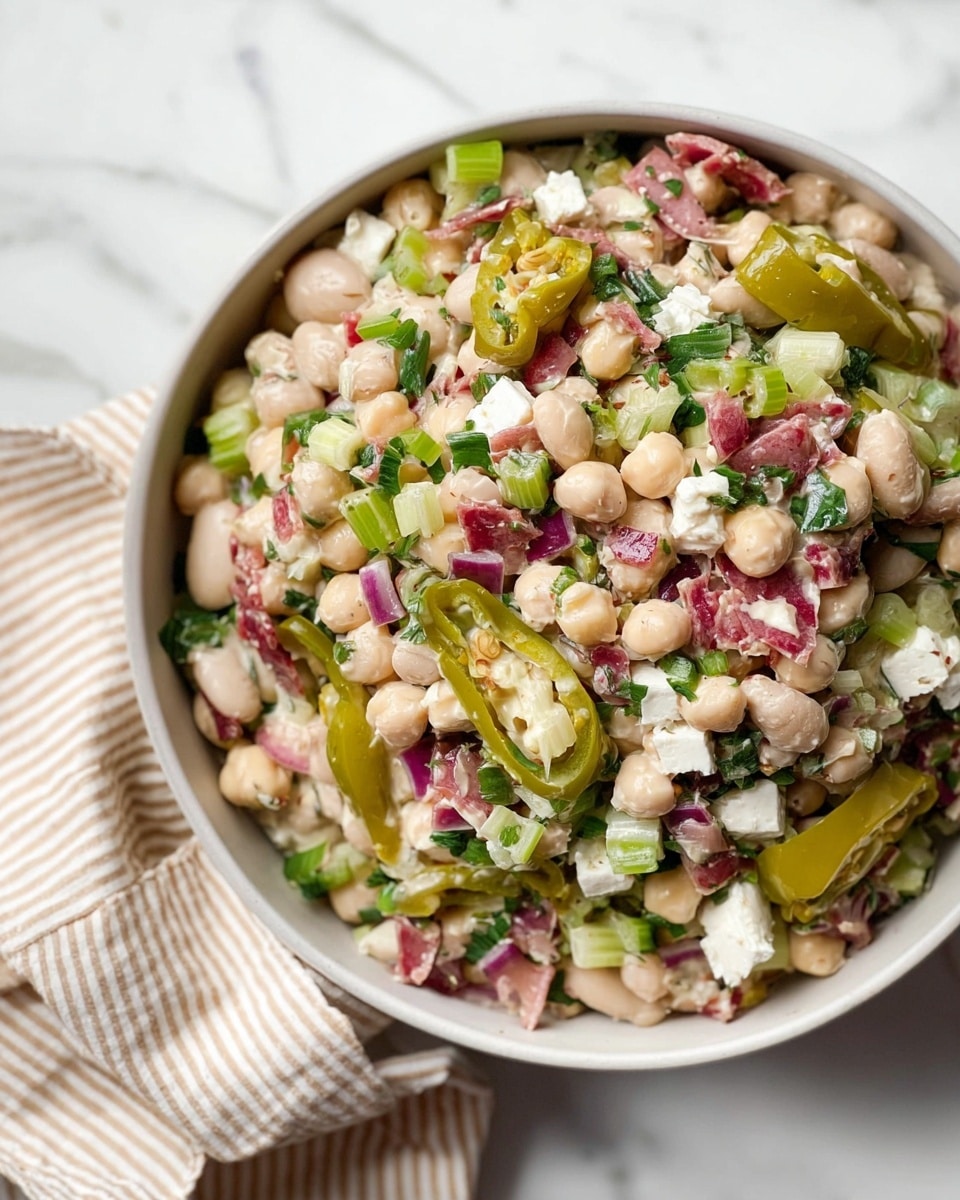 The image shows a bowl of layered bean salad placed on a white marbled surface, wrapped partly with a beige and white striped cloth. The first layer is a mix of white beans and chickpeas, creamy in texture. On top, there are chunks of white cheese and small cubes of pinkish-red cured meat, scattered evenly. Bright green herbs are sprinkled throughout, adding freshness. Light green slices of pickled peppers with a glossy look are spread over the salad. Finely chopped green celery pieces and small bits of purple onion add more color and texture. The dish is presented in a deep white bowl. photo taken with an iphone --ar 4:5 --v 7