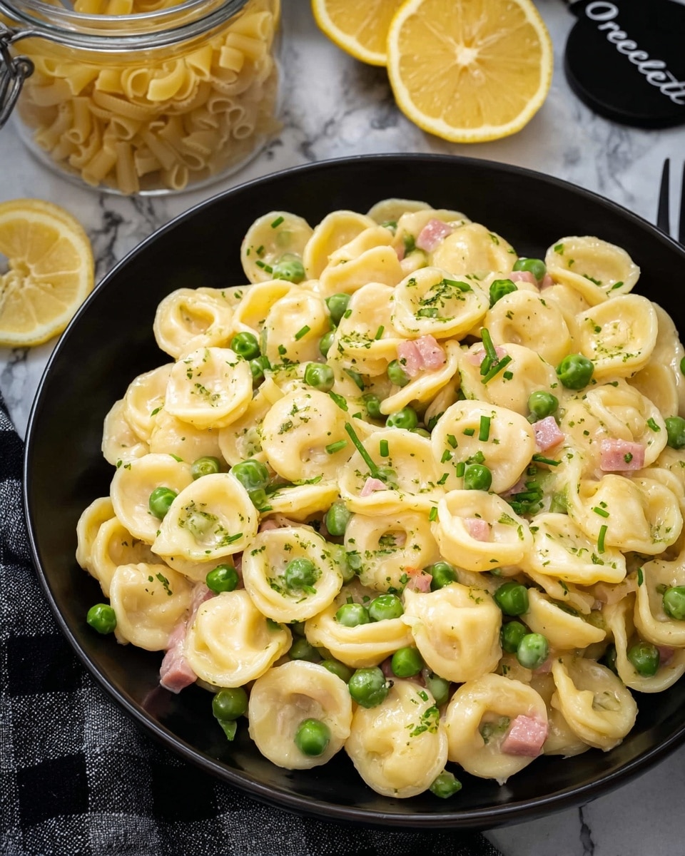 A close-up view of a black bowl filled with three layers of orecchiette pasta, creamy sauce coating the pasta giving it a shiny pale yellow color. Green peas are spread evenly in and on top of the pasta, adding bright pops of green, while small bits of pink ham are mixed throughout. Fresh green chive pieces are scattered over the dish, adding a finishing touch of color. In the background, there are two lemon halves and a glass jar filled with uncooked orecchiette pasta labeled with a black tag. The bowl is on a white marbled surface with a black and white checkered cloth partially visible at the side. Photo taken with an iphone --ar 4:5 --v 7