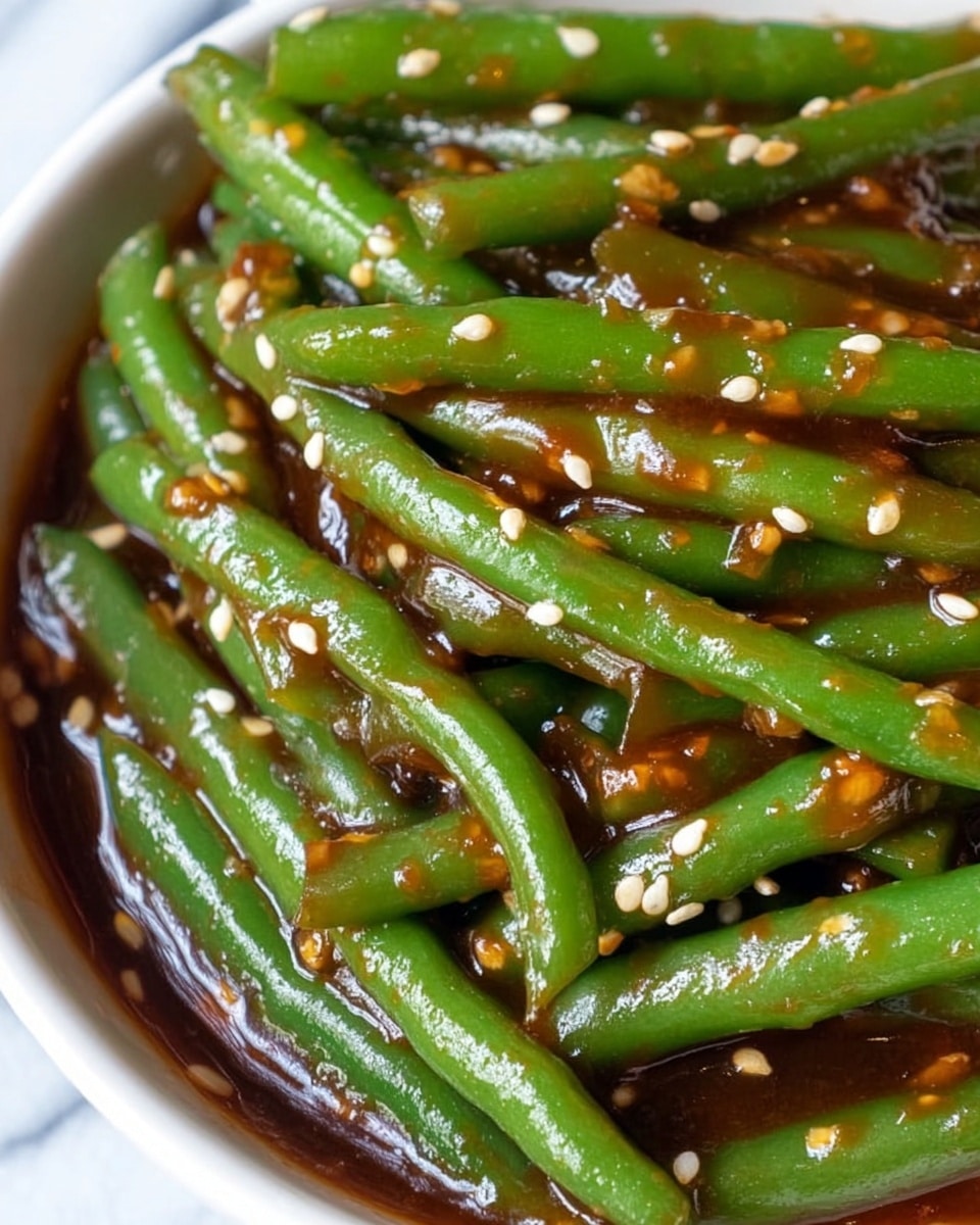 The image shows a close-up view of cooked green beans covered in a thick, shiny, dark brown sauce with visible small white sesame seeds scattered all over. The green beans are placed side by side, filling the frame, with the sauce clinging to their smooth surfaces, making the green color vibrant and fresh. The sauce texture looks glossy and slightly sticky with tiny bits that appear to be spices or minced vegetables suspended within it. The dish is in a white bowl, and the background is a white marbled texture. photo taken with an iphone --ar 4:5 --v 7