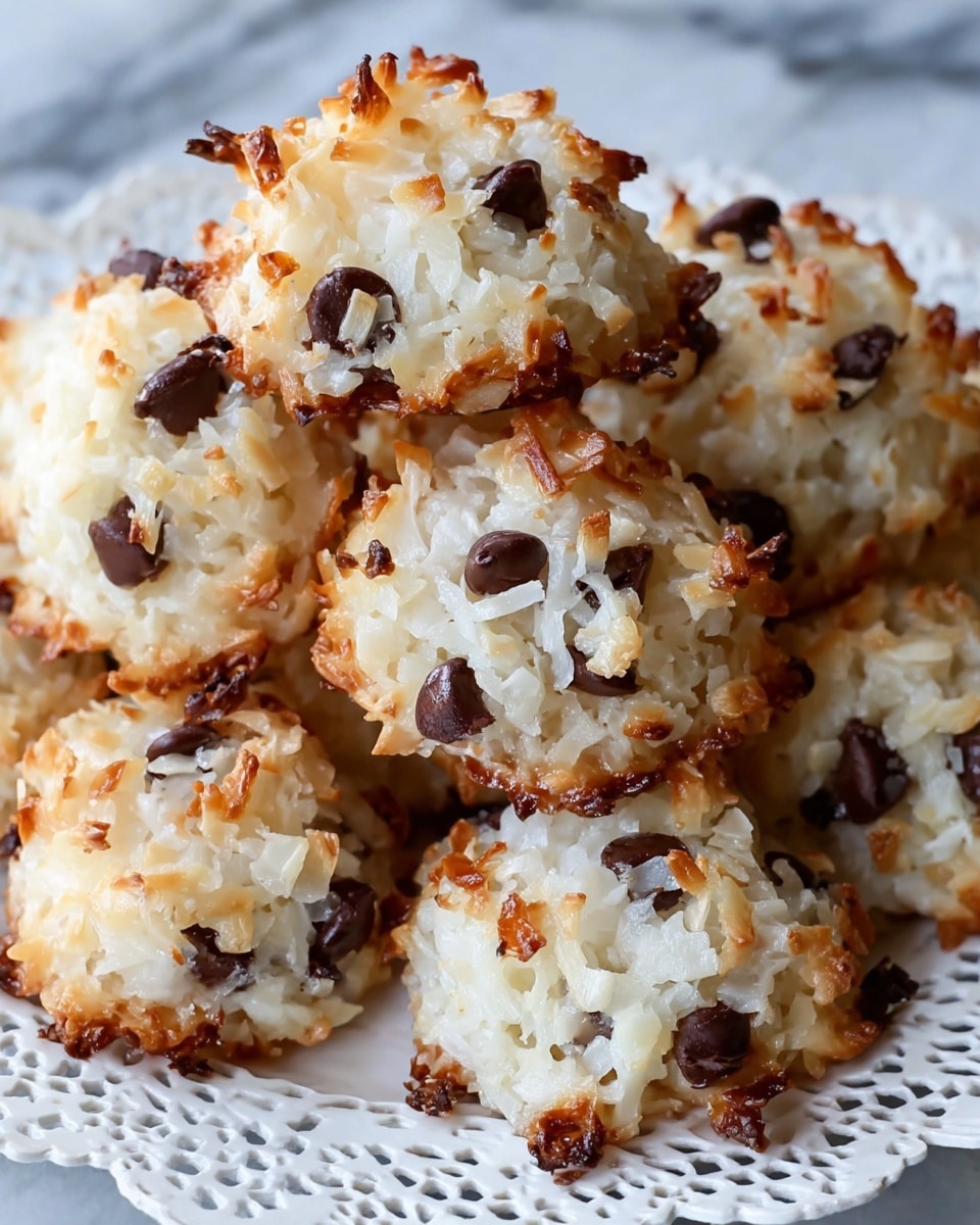 The image shows a close-up of several round coconut macaroon cookies with chocolate chips. Each cookie is textured with white shredded coconut that is slightly browned and crispy on the edges, creating a mix of light golden and white tones. The chocolate chips are scattered throughout the cookies, adding dark brown spots that contrast with the white and golden coconut. The cookies are piled together on a white plate with a delicate lace-like pattern. The background is a white marbled surface that gives a clean and bright look. photo taken with an iphone --ar 4:5 --v 7