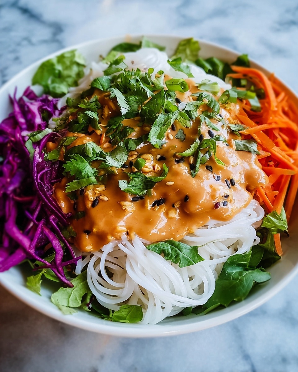 The dish shows a white bowl filled with several layers. The bottom layer is made of fresh green leaves that cover the base. On top of that, there are white rice noodles arranged in a loose pile in the center. Over the noodles, there is a thick orange-colored sauce spread unevenly, with visible black seeds mixed in. Around the noodles and sauce, there are thin strips of bright purple cabbage on the left side and thin orange carrot strips on the right. Fresh green herbs are sprinkled generously on top of the sauce and noodles. The bowl sits on a white marbled surface. photo taken with an iphone --ar 4:5 --v 7