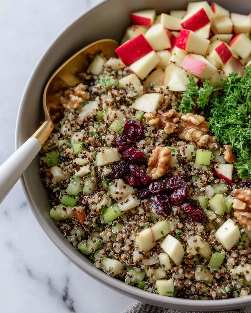 A large bowl filled with a mixed quinoa salad showing three main layers: the base is light beige quinoa seeds with a slightly fluffy texture, mixed evenly with small chopped green celery pieces that add a fresh crunch. On top of this are small cubes of red and yellow apple pieces, scattered around giving bright red and pale yellow pops of color. Dark brown raisins and some crunchy walnut pieces are mixed throughout, creating texture contrast. Finely chopped green parsley is sprinkled all over the salad, adding a fresh green color. The bowl is placed on a white marbled surface with parts of a white cloth and small wooden bowl of salt visible around. Photo taken with an iphone --ar 4:5 --v 7