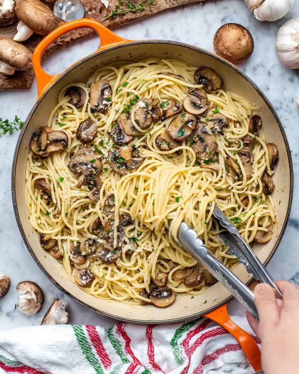 A large pan with orange handles holds a dish of spaghetti mixed with sautéed mushroom slices. The spaghetti noodles are pale yellow and form the base layer, with the mushrooms scattered evenly on top, showing a brown and slightly golden color from cooking. Small bits of green herbs are sprinkled across the pasta and mushrooms, adding spots of fresh color. A woman's hand is holding metal tongs, lifting a portion of the spaghetti near the right side of the pan. The pan is set on a white marbled surface with a white cloth showing red and green stripes underneath the handle, and around it are some whole mushrooms, garlic bulbs, and a wooden cutting board with herbs. photo taken with an iphone --ar 4:5 --v 7
