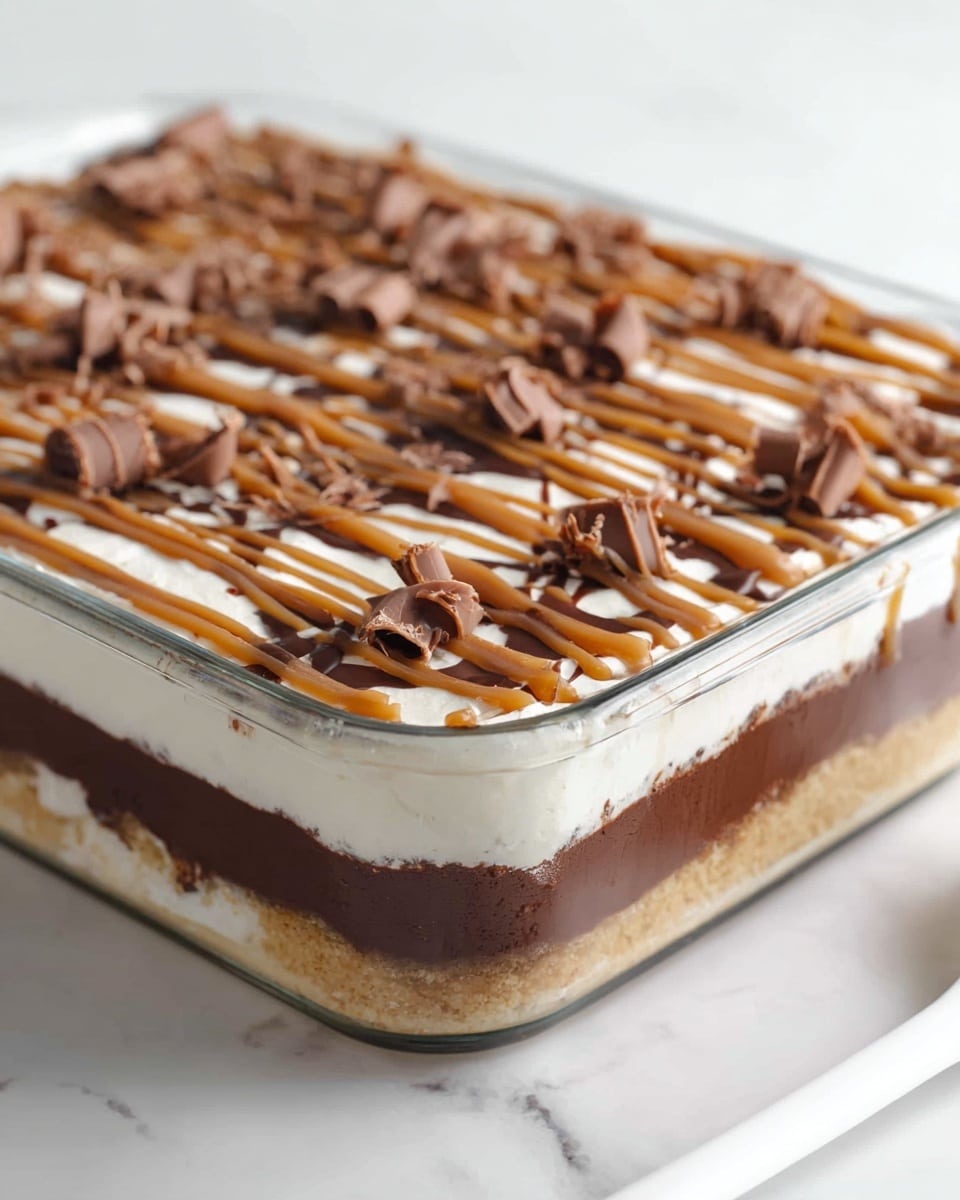A clear glass rectangular dish showing three main layers: the bottom layer is a light beige crumb base, the middle layer is a thick, dark brown chocolate layer, and the top layer is a smooth white cream. The cream layer is decorated with thin drizzles of light brown sauce in a crisscross pattern, topped with small curls of milk chocolate spread evenly across the surface. The dish is set on a white marbled texture, with a white spoon partially visible on the right side. photo taken with an iphone --ar 4:5 --v 7
