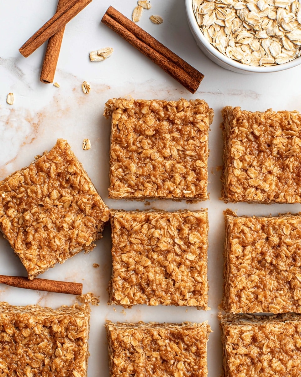 The image shows a close-up of nine oatmeal bars arranged in a grid pattern on a white marbled surface, each bar having a single thick layer composed of visible oats mixed with a golden brown binding ingredient, giving them a rough and chewy texture. Two pairs of cinnamon sticks are placed diagonally on the top left and bottom right corners of the bars, adding a warm brown contrast. A small white bowl filled with oats is partially visible in the top right corner, complementing the scene with a light natural touch. photo taken with an iphone --ar 4:5 --v 7