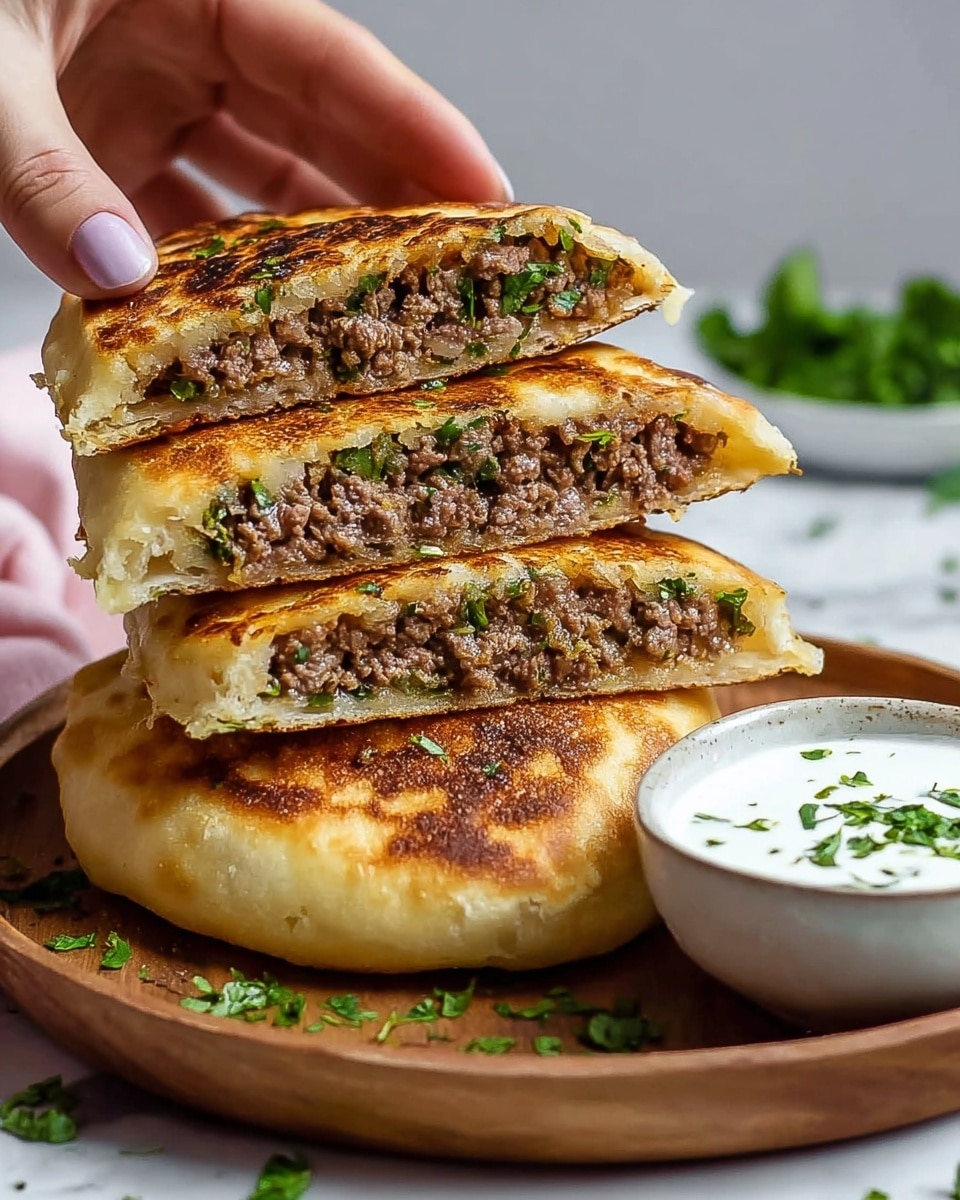 A stack of three thick flatbread sandwiches filled with a cooked, crumbly ground beef mixture with finely chopped green herbs is shown on a round white plate. The flatbreads have a golden-brown toasted crust with a slightly crispy texture. The sandwiches are cut in half, exposing two layers of light, fluffy white dough enclosing the brown, herb-speckled meat filling. A small white bowl filled with creamy white sauce with green herb pieces sits on the plate next to the stacked sandwiches. The entire setting is on a white marbled surface, and a woman's hand is lifting the top sandwich half. photo taken with an iphone --ar 4:5 --v 7
